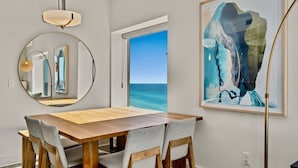 Un comedor con una mesa de madera y sillas tapizadas en gris, un espejo redondo y un cuadro abstracto grande en la pared.
