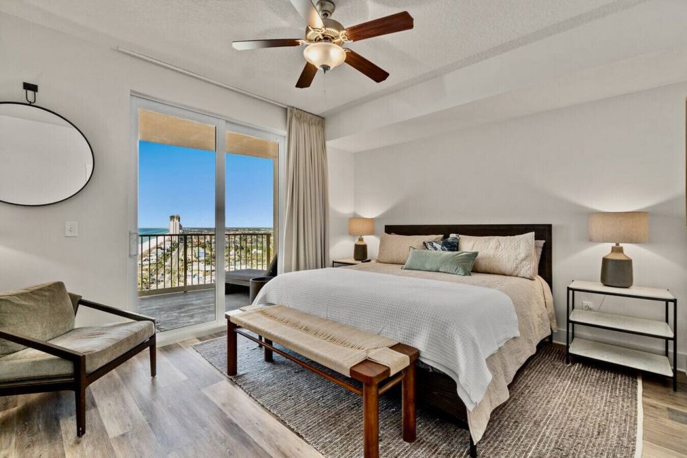 A bedroom with a large bed, a bench, a chair, a nightstand, and a ceiling fan.