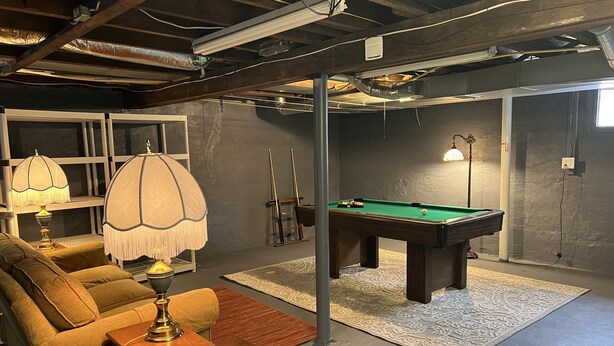 Une pièce confortable avec une table de billard, un canapé et une lampe.