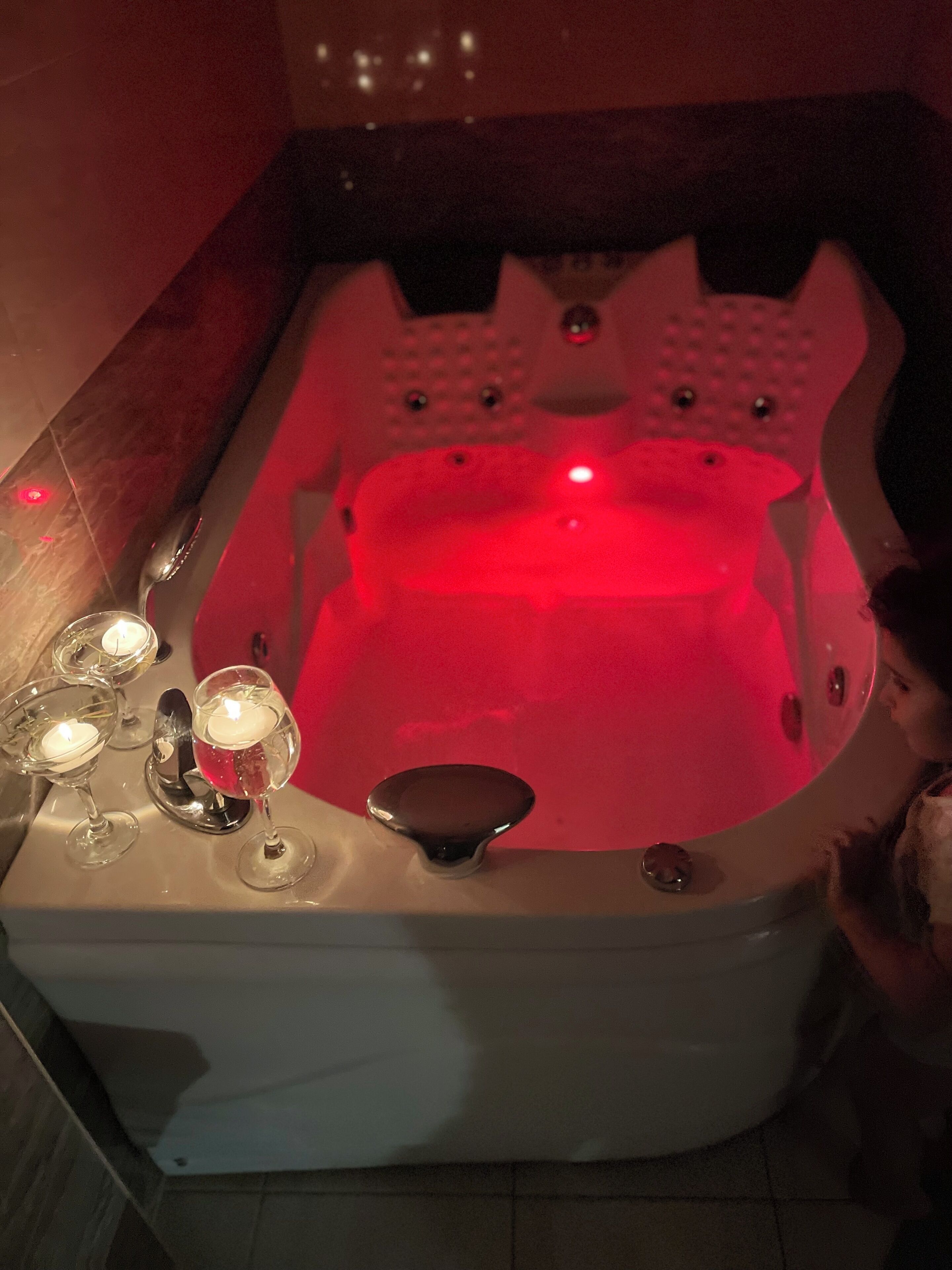 A hot tub with a red light, surrounded by candles and glasses.