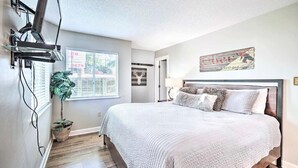 A bedroom with a large bed, a potted plant, a wall-mounted TV, and a window with blinds. - Gorgeous 2BD Condo w Balconies + Pool! Near TOWN! (Gatlinburg)