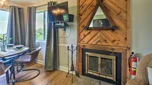 A cozy room with a fireplace, a television mounted on the wall, a dining table with chairs, and a window with curtains. - Gorgeous 2BD Condo w Balconies + Pool! Near TOWN! (Gatlinburg)