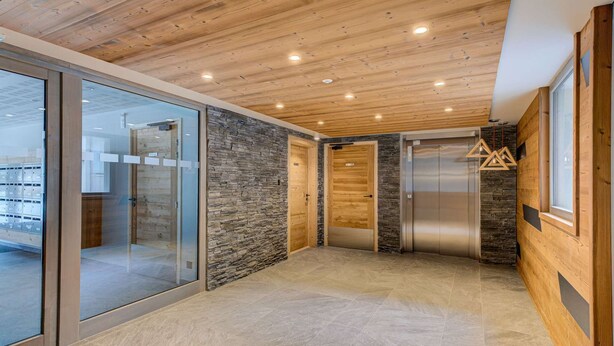 Un interior moderno con techo de madera, pared de piedra, puertas de cristal y un ascensor metálico.