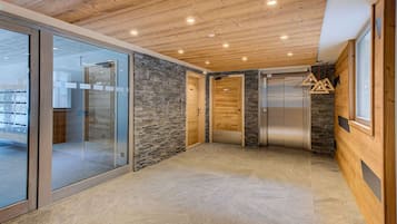 A modern interior with wooden ceiling, stone wall, glass doors, and a metal elevator.