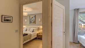 Un dormitorio con cama, mesitas de noche, un cuadro y vistas a través de una puerta abierta.
