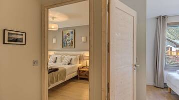 A bedroom with a bed, bedside tables, a painting, and a view through an open door.