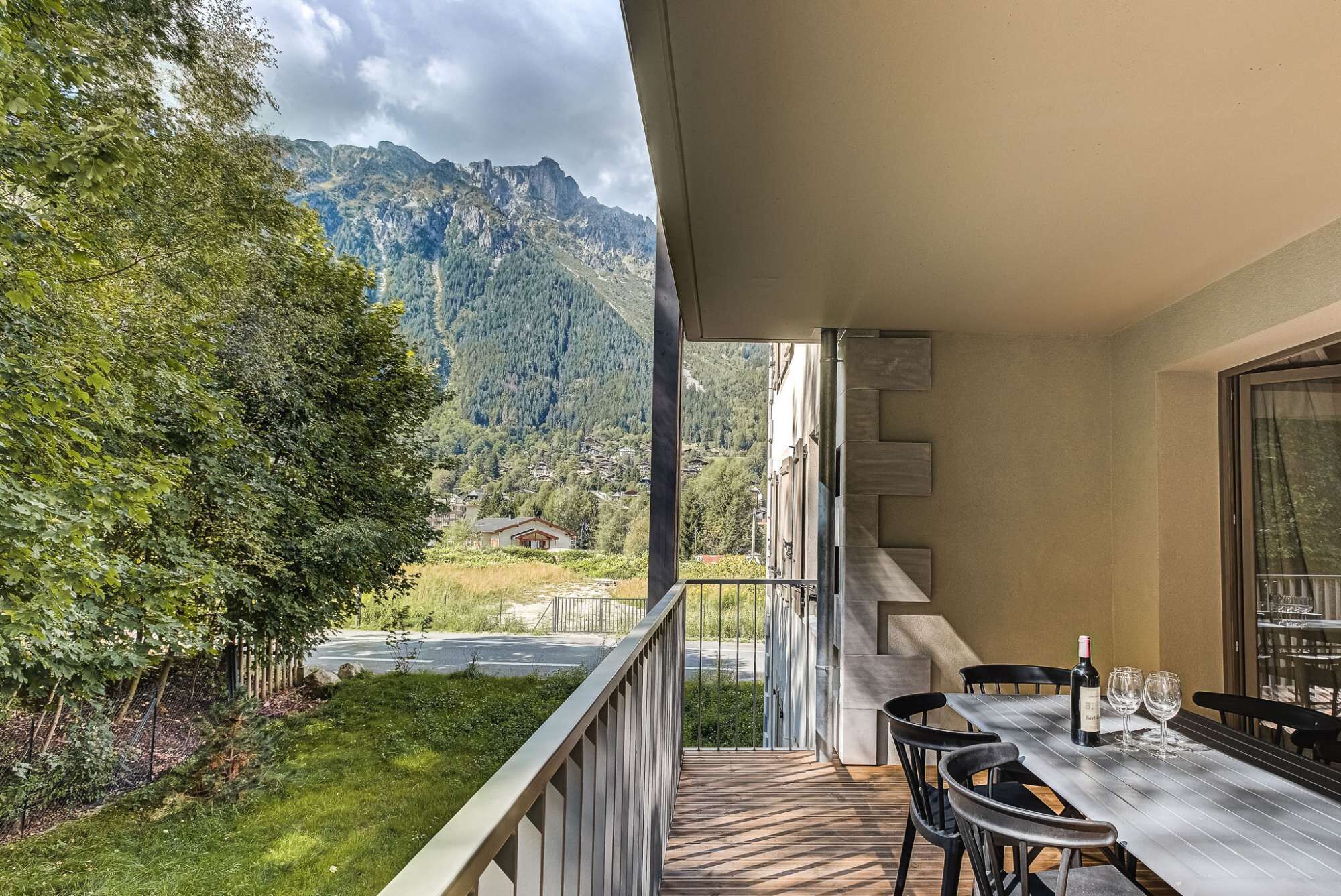 Un balcon avec une table et des chaises, donnant sur un paysage montagneux avec une route et de la végétation.