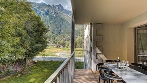 Un balcón con mesa y sillas, con vistas a un paisaje montañoso que incluye una carretera y vegetación.