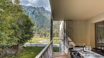 Un balcon avec une table et des chaises, donnant sur un paysage montagneux avec une route et de la végétation.