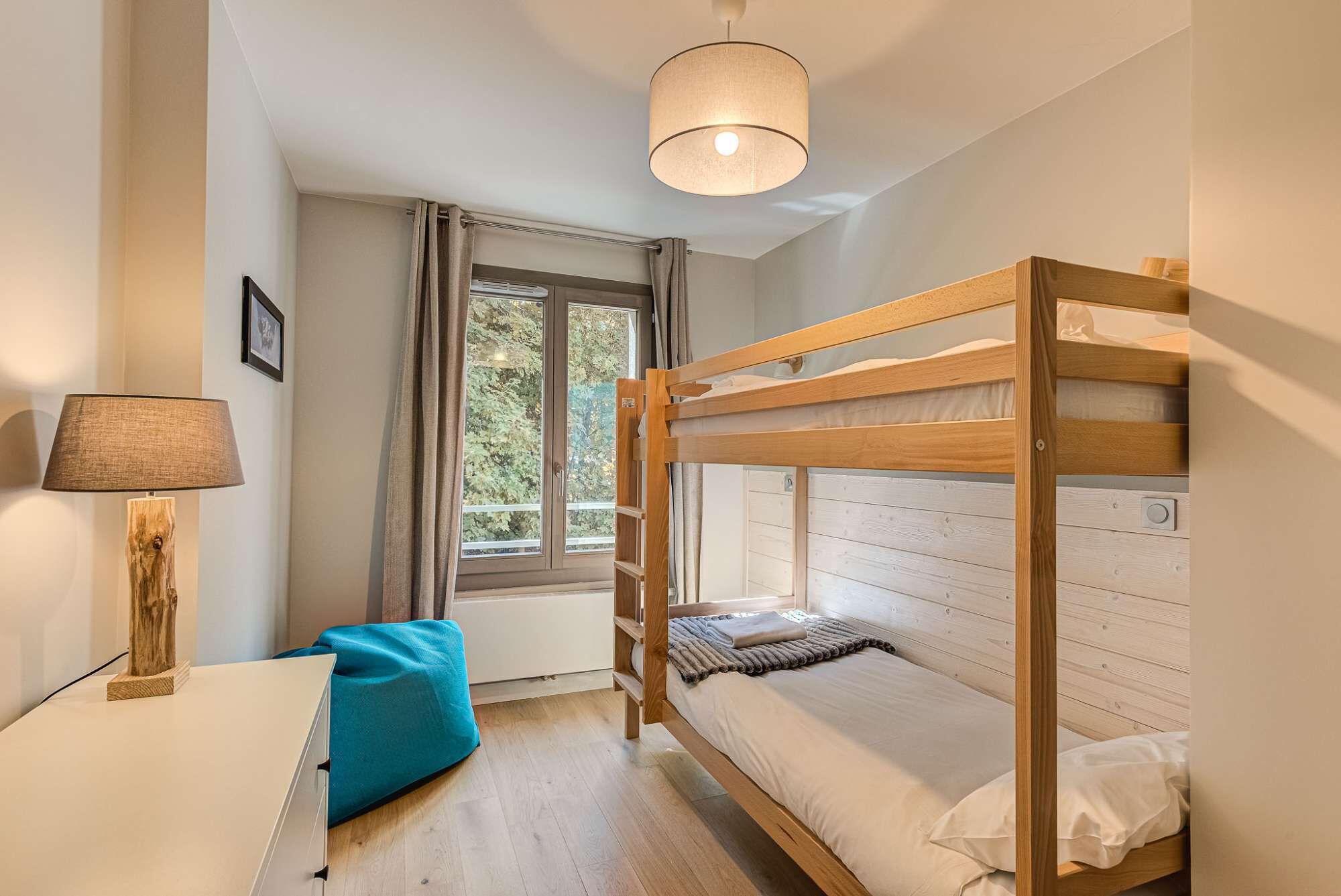 A bunk bed room with a window, a desk, and a lamp.