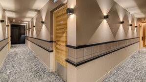 Pasillo de hotel con una puerta de madera con la etiqueta 'ESCALER', alfombra estampada e iluminación en la pared.