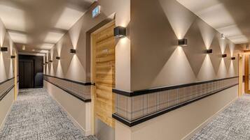 A hotel corridor with a wooden door labeled "ESCALER," a patterned carpet, and wall-mounted lighting.
