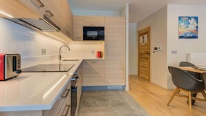 Una cocina moderna con microondas integrado, un hervidor rojo y un tostador. Hay una puerta de madera y un cuadro en la pared.