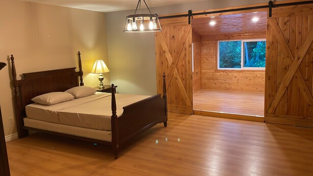 A bedroom with a wooden bed, a nightstand with a lamp, and a view of the outdoors through a wooden door. - Parkhill / GrandBend - Spanish Style Private Acerage property (Parkhill)