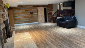A spacious living room with a wooden floor, a black leather sofa, and a stone fireplace. - Parkhill / GrandBend - Spanish Style Private Acerage property (Parkhill)