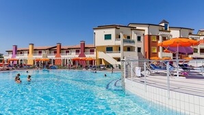 A swimming pool with lounge chairs and umbrellas, surrounded by multi-story buildings with balconies.
