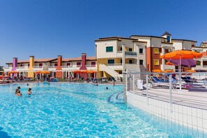 A swimming pool with lounge chairs and umbrellas, surrounded by multi-story buildings with balconies.