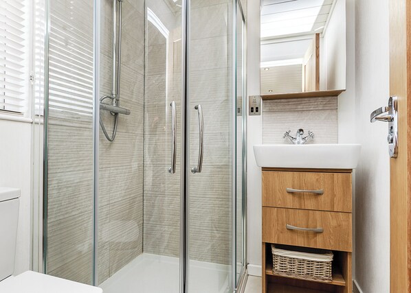 Un baño moderno con ducha envuelta en vidrio, un lavabo blanco y muebles de madera.