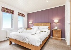 A bedroom with a wooden bed, two bedside tables, a nightstand, a window with a view, and a wall-mounted lamp. - 4 bedroom accommodation in Newton Saint Loe, Nr Bath (Newton Saint Loe, Nr Bath)