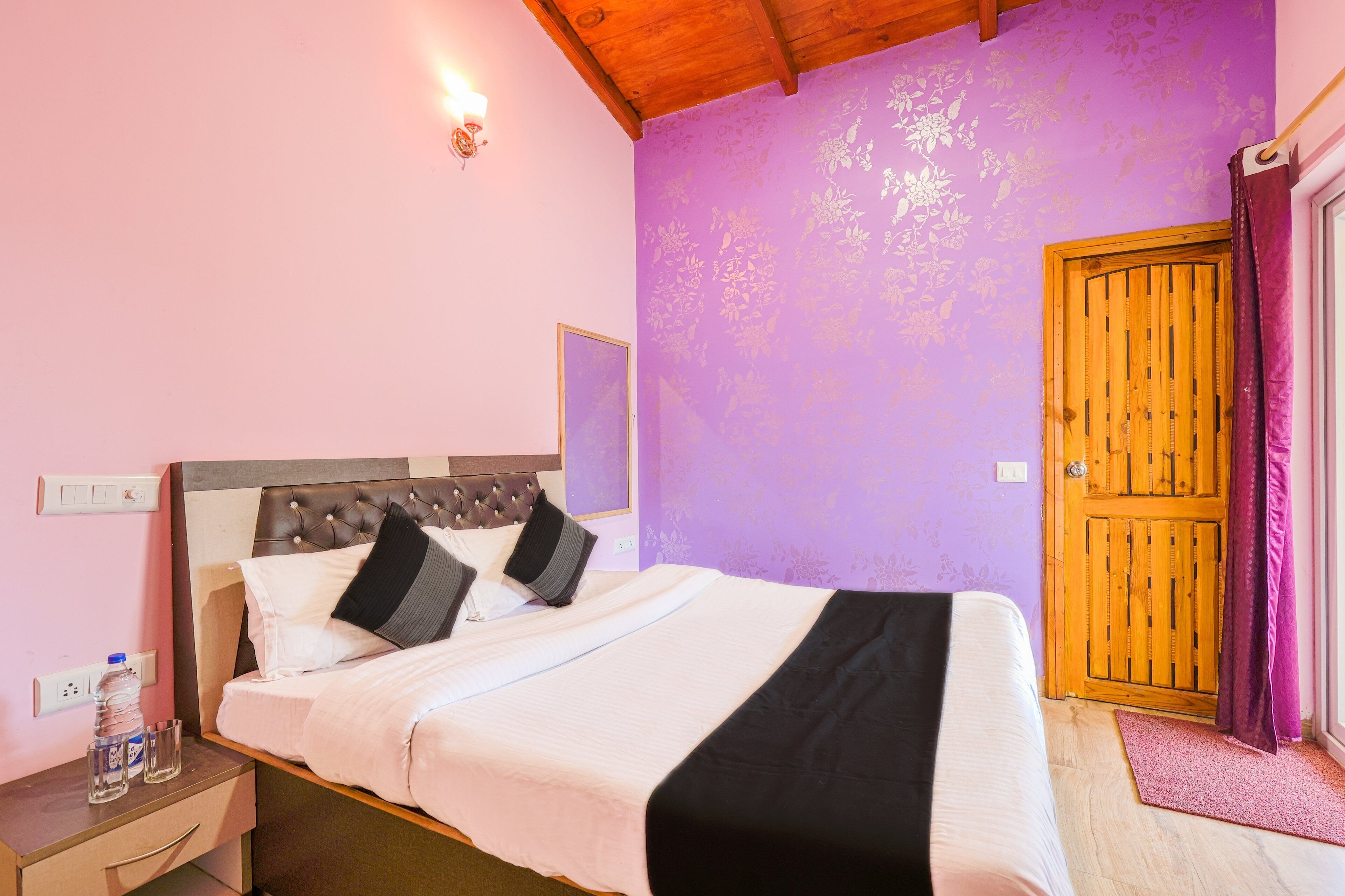 A bedroom with a bed, a nightstand, a wooden door, and a purple wall.
