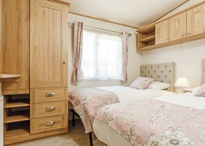 Quarto com duas camas, guarda-roupa, janela com cortinas e mesa de cabeceira com abajur.