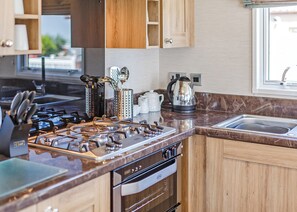 Uma cozinha moderna com fogão a gás, eletrodomésticos de aço inoxidável, armários de madeira e bancada de mármore.