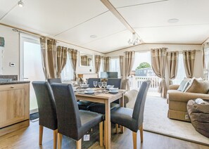 Un coin repas avec une table dressée pour quatre personnes, un canapé et un téléviseur, dans une pièce agrémentée de rideaux et d’un lustre.