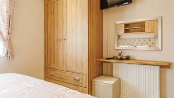 A bedroom with a wooden wardrobe, a television mounted above a mirror, a bedside table, and a radiator.