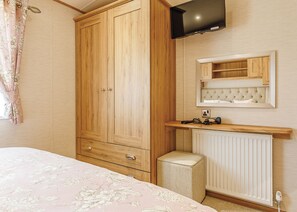 Une chambre à coucher avec une armoire en bois, un téléviseur fixé au-dessus d’un miroir, une table de chevet et un radiateur.