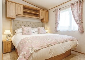Une chambre à coucher avec un lit, des tables de chevet, une tête de lit en bois et une fenêtre avec des rideaux.