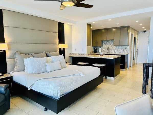 A modern bedroom with a large bed, a ceiling fan, and a kitchen area with a marble countertop.