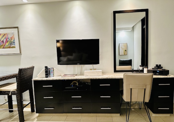 A modern bathroom with a large mirror, a flat-screen TV, and a vanity with drawers.
