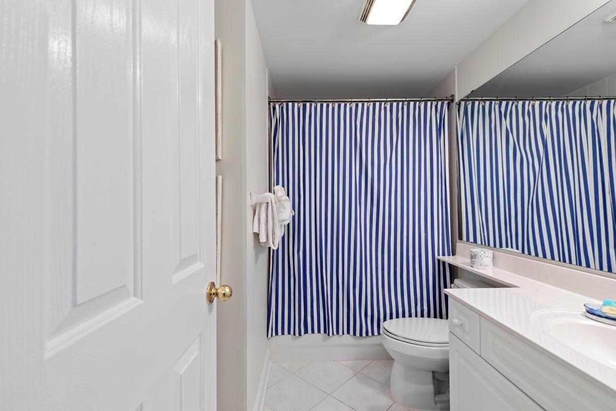 A bathroom with a white door, a white toilet, a white sink with a mirror, and a blue and white striped shower curtain.