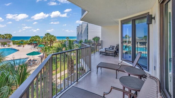 Een balkon met uitzicht op een zwembad en strand, voorzien van stoelen en een tafel.