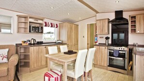Una cucina compatta con zona pranzo, mobili in legno, forno a microonde, fornello e finestra con tende.