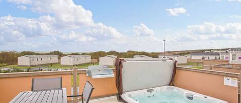 A deck with a hot tub, a table, and chairs, overlooking a residential area with houses.