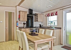 A compact kitchen with wooden cabinets, a stove, and a dining area with chairs.