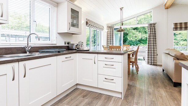 A modern kitchen with white cabinetry, a built-in stove, and a dining area with a wooden table and chairs. - 1 bedroom accommodation in Newton Saint Loe, Nr Bath (Newton Saint Loe, Nr Bath)