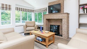 A modern living room with a fireplace, comfortable seating, and large windows. - 1 bedroom accommodation in Newton Saint Loe, Nr Bath (Newton Saint Loe, Nr Bath)