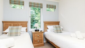 A double room with two beds, a nightstand, a lamp, and a window with a view of greenery. - 1 bedroom accommodation in Newton Saint Loe, Nr Bath (Newton Saint Loe, Nr Bath)