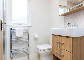 A bathroom with a white toilet, a chrome towel rack, a wooden vanity with a sink, and a window above the toilet. - 3 bedroom accommodation in Newton Saint Loe, Nr Bath (Newton Saint Loe, Nr Bath)