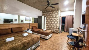 A hotel room with a wooden floor, two beds with brown bedding, a desk with a chair, a ceiling fan, and a door leading to a balcony. - Hotel Urban-Khotel Kurban Hotel (Baguio)