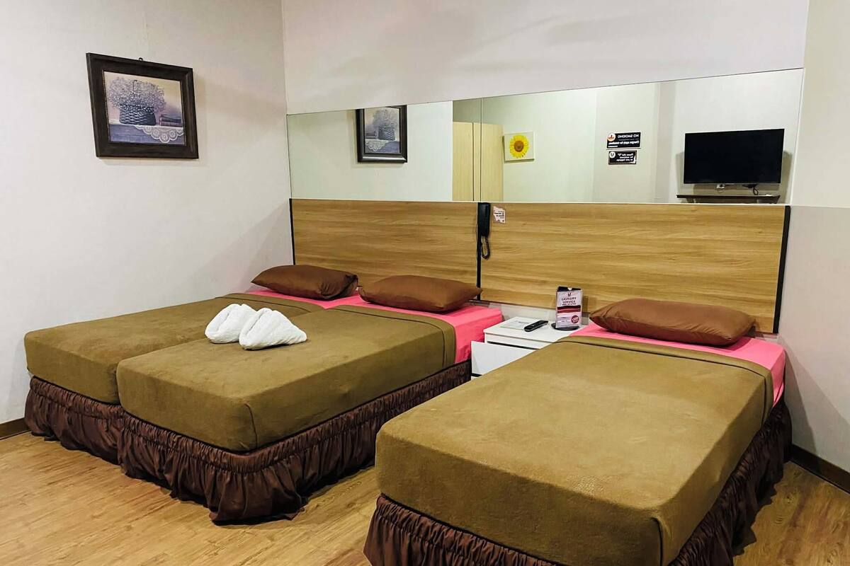 Une chambre d’hôtel avec deux lits, chacun recouvert d’une couverture marron et agrémenté d’oreillers assortis. On y trouve une petite table avec une télécommande et un panneau indiquant la présence d’un service de blanchisserie.