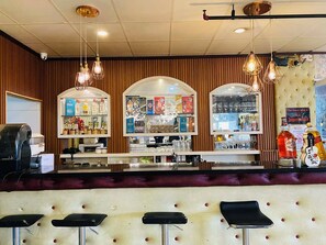 A bar area with stools, a counter with various bottles, and hanging lights.