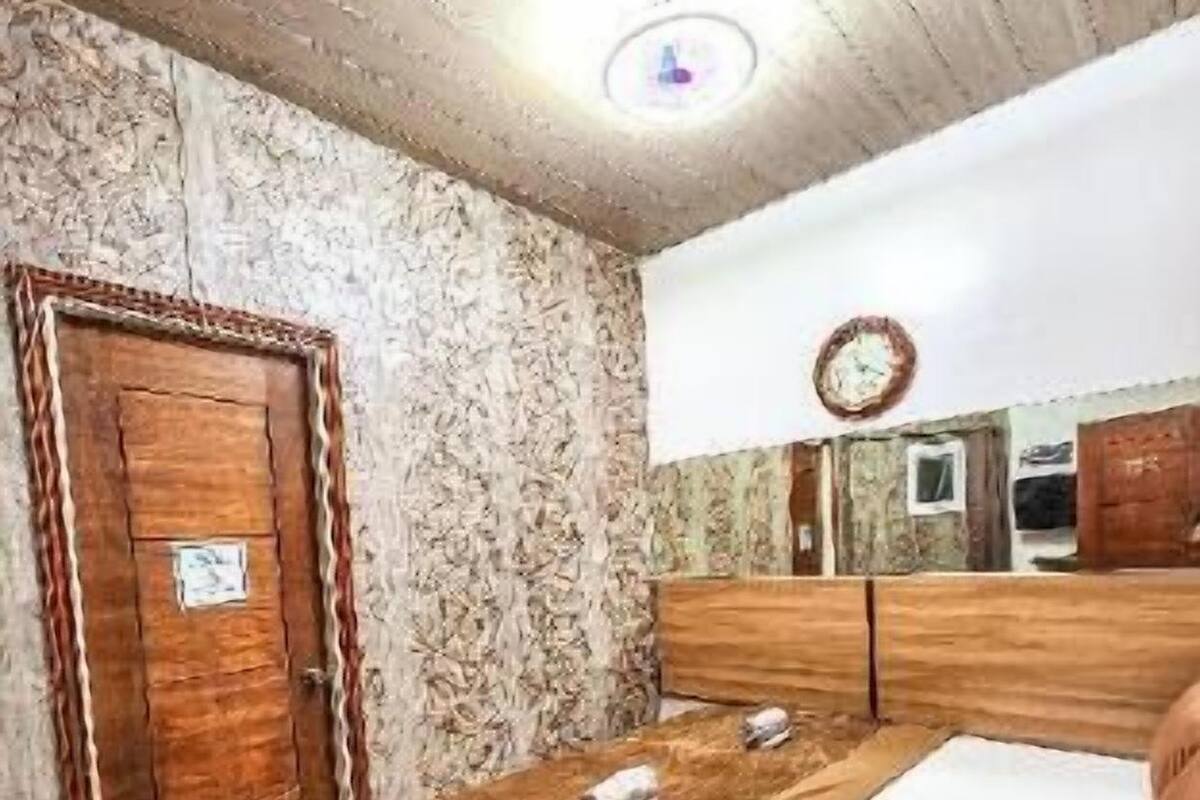 Une pièce avec un lit en bois, une porte en bois, un miroir et une horloge au mur.