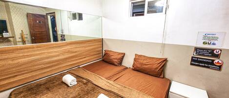 A hotel room with a bed, a small bedside table, a mirror, and a window. There are signs on the wall about water conservation and no smoking.