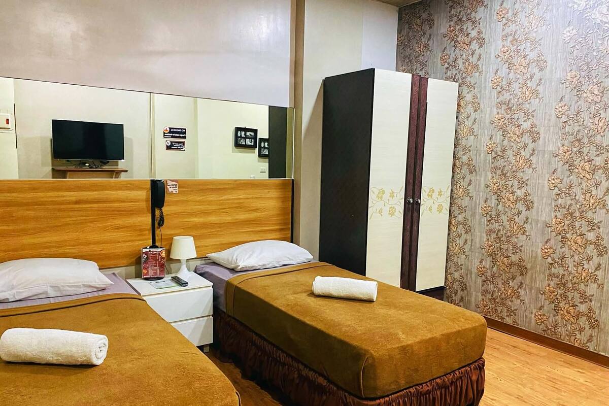 Une chambre d’hôtel avec deux lits, une armoire, un bureau avec une lampe, une télévision et un miroir.