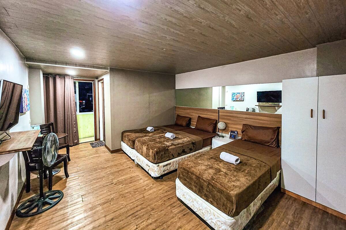 Une chambre d’hôtel avec deux lits, un bureau avec une chaise, un ventilateur et une armoire.