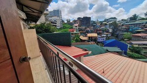 A balcony with a metal railing overlooking a densely packed urban area with various buildings and a clear sky. - Hotel Urban-Khotel Kurban Hotel (Baguio)