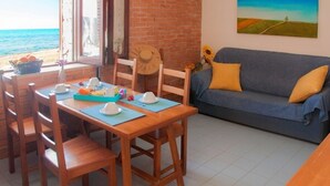 A dining area with a table set for breakfast, a blue sofa with yellow cushions, a painting of a landscape, and a view of the sea through a window. - Apollo's Terraces Beach apartments less than 20 m from the sea!Sirocco (Marinella di Selinunte)